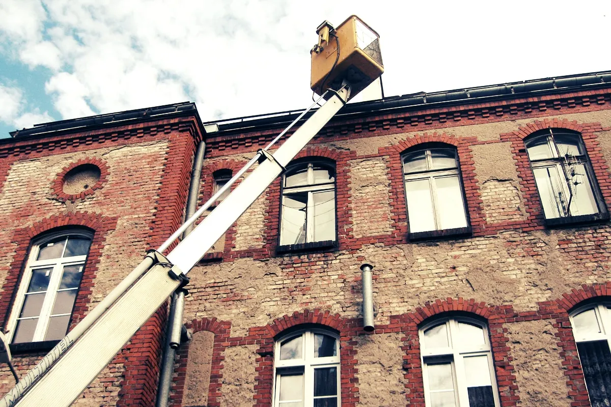 Podnośnik koszowy Firmy Haker rozłożony przy elewacji ceglanej kamienicy